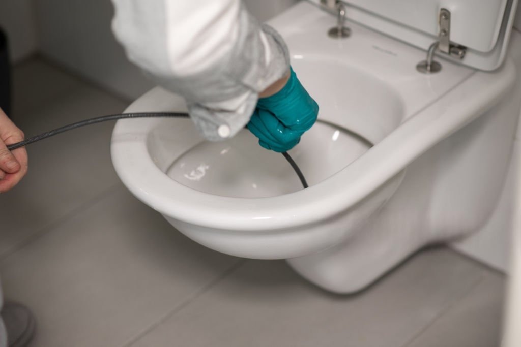 Drain cleaning in Highland by Summit Plumbing Pros with a technician clearing a toilet drain using a drain snake.