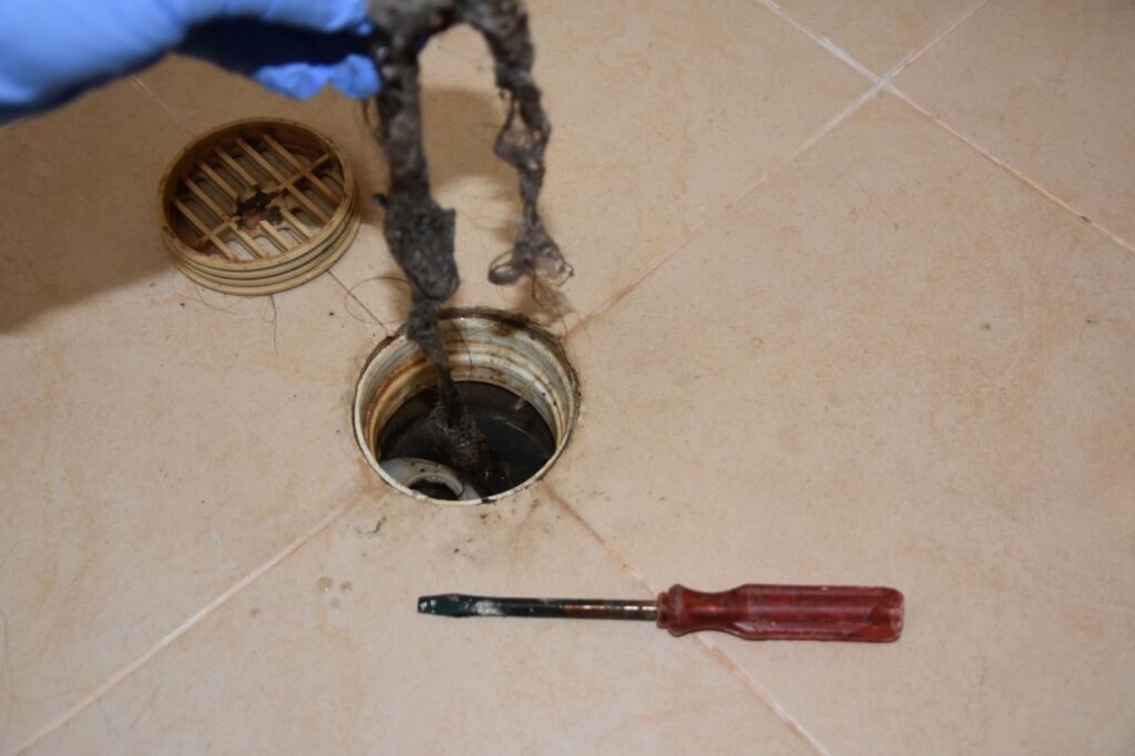 Drain cleaning in Elk Ridge with a gloved hand removing hair and debris from a floor drain by Summit Plumbing Pros.