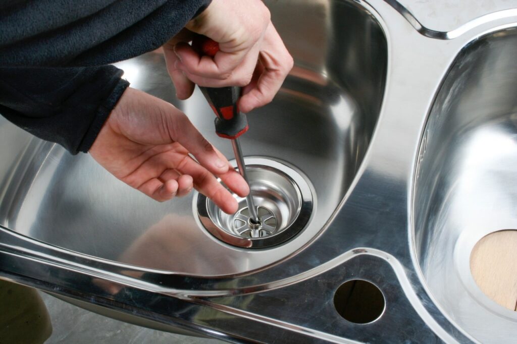 Drain cleaning in Woodland Hills with a technician using a screwdriver to service a kitchen sink drain by Summit Plumbing Pros.