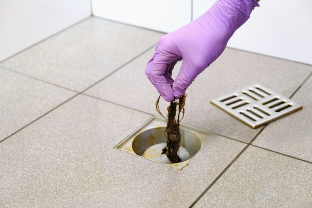 Drain cleaning in Cottonwood Heights with a glipped hand removing hair and debris from a floor drain by Summit Plumbing Pros.