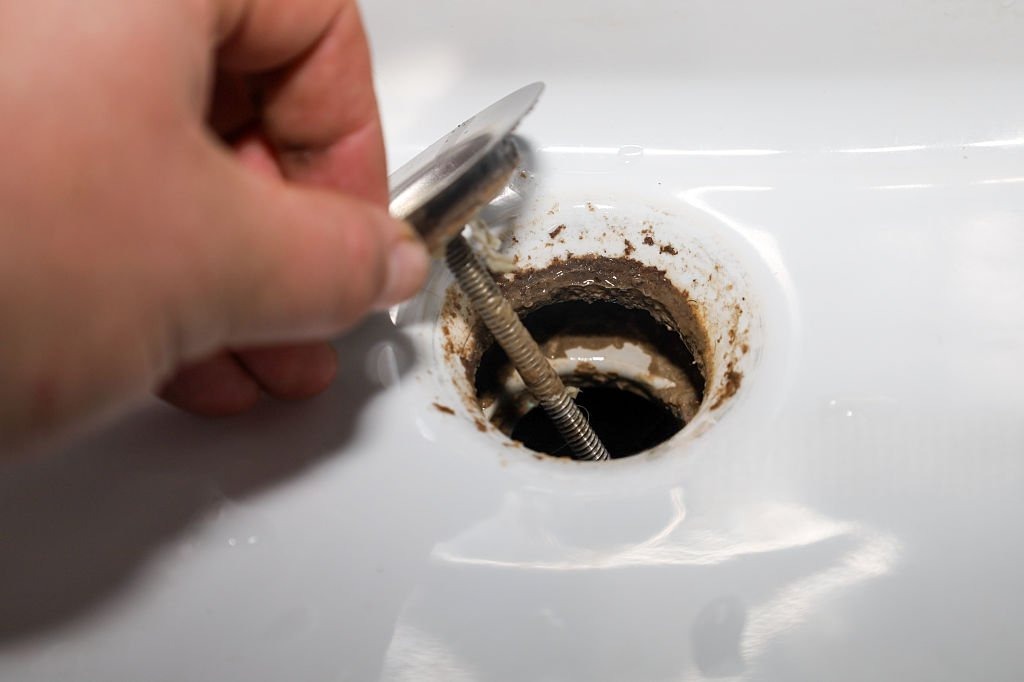 General plumbing services in Alpine with a sink stopper being removed from a dirty drain opening